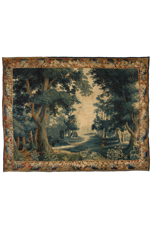 This image features a French Verdure tapestry, showcasing an intricate woodland scene with lush trees, dense foliage, and a serene, sunlit clearing in the background. The tapestry is bordered by a detailed floral pattern, enhancing its classical elegance. The deep, rich greens and earthy tones are characteristic of 17th-century Verdure tapestries. This wall hanging exemplifies the masterful weaving techniques and artistic finesse typical of the Baroque period's textile art. Ideal for those interested in ant